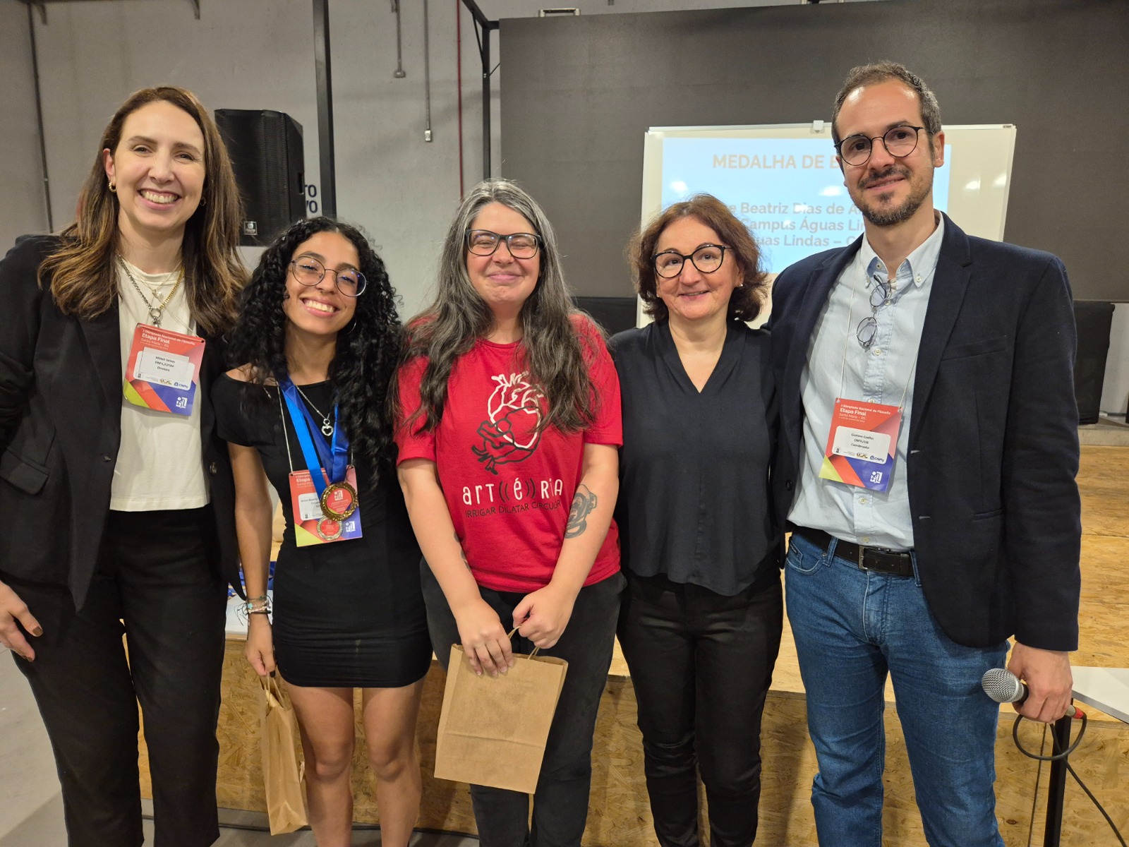 Anne recebendo a medalha de bronze da etapa final acompanhada da profa. Alice e com profa. Mitieli Seixas (UFSM) e Gustavo Coelho (CIB) - idealizadores e organizadores da I Onfiil - e com a profa. Solange Dejeanne (UFN), jurada na etapa nacional